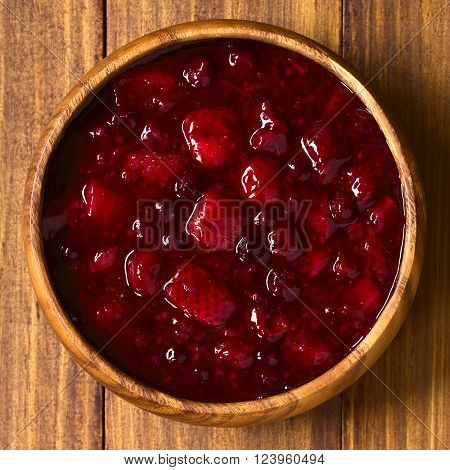 German Rote Gruetze (red groats) red berry pudding made of strawberry, blueberry, raspberry and redcurrants cooked with sugar and starch, photographed overhead on wood with natural light