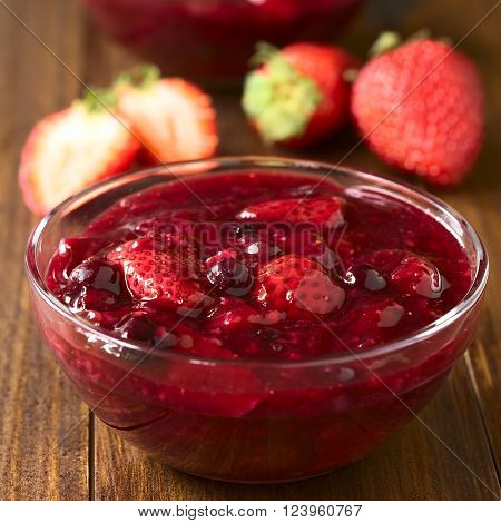 German Rote Gruetze (red groats) red berry pudding made of strawberry, blueberry, raspberry and redcurrants cooked with sugar and starch, photographed on wood with natural light (Selective Focus, Focus one third into the dessert)
