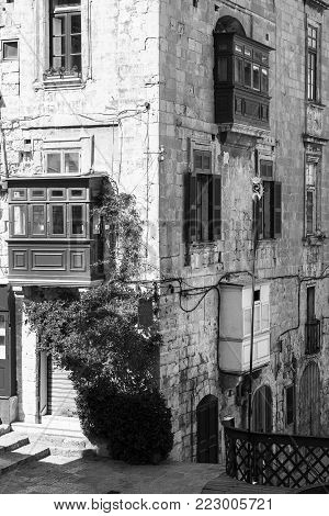 Building with traditional colorful maltese balcony in historical part of Valletta. Red windows decoreted with begonville on the facade of a house in Malta. Black and white picture