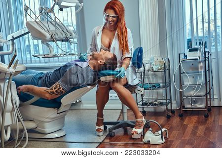A Sexy hot redhead dentist woman, at work in the office, taking care of her patient.