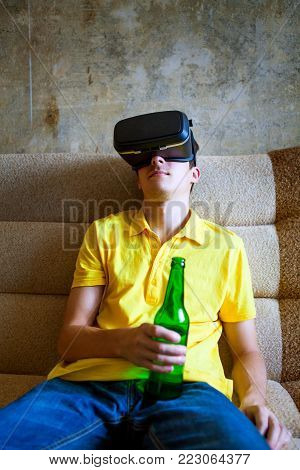 Young Man in VR Glasses hold Bottle of a Beer on the Sofa
