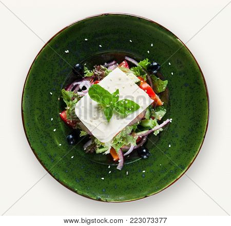 Fresh vegetable salad with feta cheese on green plate isolated over white background, top view. Maditerranean cuisine, mockup and cutout for restaurant menu