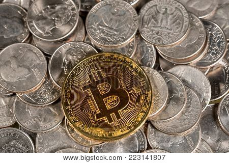 Single golden bitcoin coin laid on loose change of US quarters