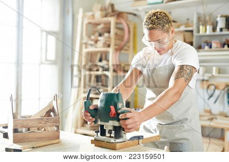 Woman with electric grinder processing wooden boards in workshop