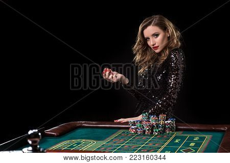 Sexy woman in a black dress playing in casino. Woman stakes piles of chips playing roulette at the casino club. Gambling. Roulette.