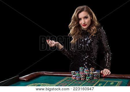 Sexy woman in a black dress playing in casino. Woman stakes piles of chips playing roulette at the casino club. Gambling. Roulette.