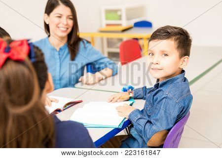 Portrait of a handsome Hispanic preschool student sitting at class and working on a writing assigment