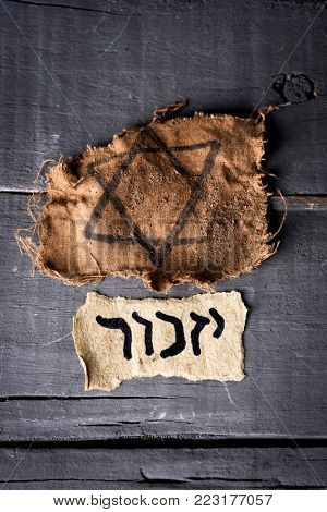 high angle view of a ragged jewish badge and a yellowish piece of paper with the word yizkor, remember in hebrew and the name of a prayer in memory of deceased beloveds, on a rustic wooden surface