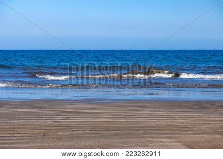 Waves of the ebbing sea crash over the wet sand of the empty beach
