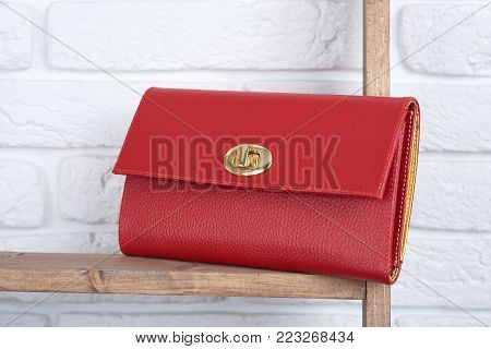 Red woman s leather clutch laying on the wooden shelf on white wall background in the shop. Perfect for everyday casual look and for pretty cocktail dress.