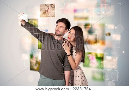 Collecting memories concept with photos in backbround and a happy young couple in love taking selfie with a mobile phone
