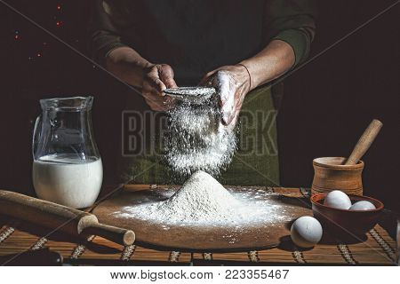 Preparation of bread dough. Bakery, baker's hands, flour is poured, flying flour. toned