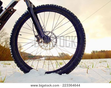 Front wheel of mountain bike stay in snow. Snow flakes melting on dark off road tyre.  Winter weather in the field.