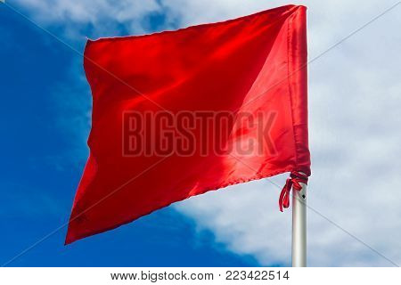 Red warning flag at the beach with blue sky background