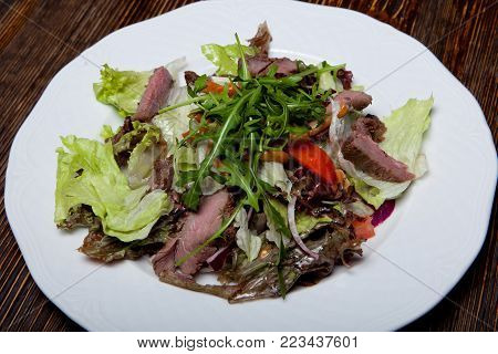 wild boar meat salad, pickled cabbage, blue onion, mix of salads, fresh tomatoes on a black table