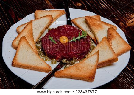 Fried tartar meat dish with yolk and a crown on a black wooden background