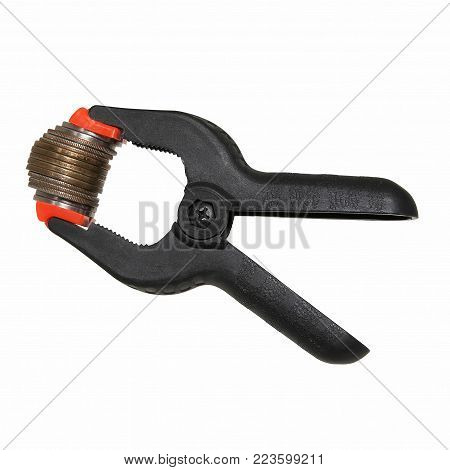 A black clamp holding silver coins at white background