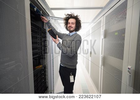 young IT technician using digital cable analyzer on server in large data center