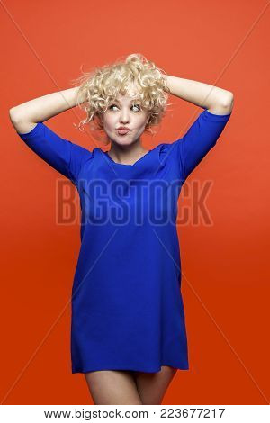Beautiful curly blonde girl sitting on orange background