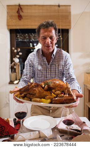 Beautiful big family sitting at the table celebrating Christmas together at home. Father bringing roasted turkey on a serving tray.