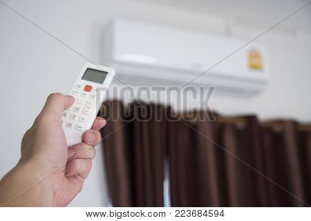 A man use remote controller to set air conditioner temperature in the room.Hand holdind control remote switch of home air conditioner