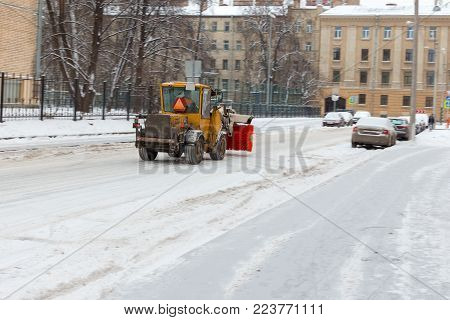 yellow snow-removing machine with a red brush rides down the city street