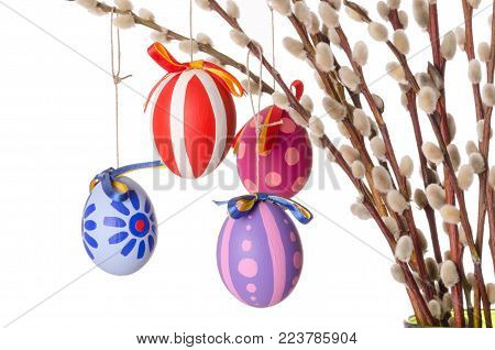 Easter eggs on willow bouquet with catkins, horizontal. Four hand-painted colored Paschal eggs on branches of sallows or also called osiers, with aments. Photo on white background.