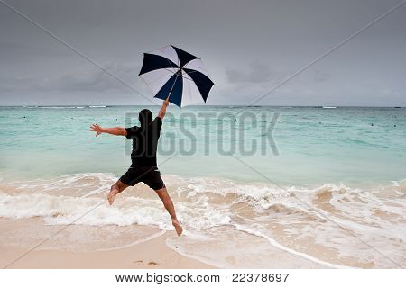 Opálený muž skok s deštníkem v modré moře pod šedou oblohou