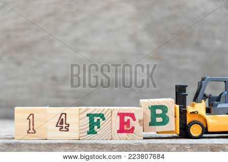 Toy forklift hold letter block B to complete word 14 Feb on wood background (Concept for 14 february that is Valentine 's day)