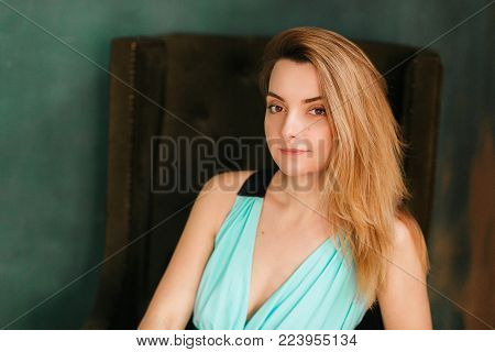 Portrait of the beautiful woman sitting in a chair and looking straight. Close-up shot. Loft green wall on background