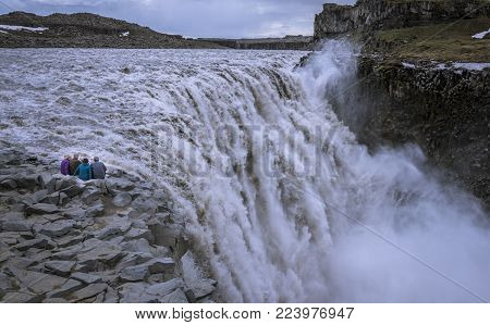 Senior travelers sitting on the edge, contemplating Detifoss waterfall. Retirees traveling arround the world.