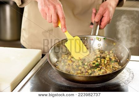 Cooking vegetables in pan using utensil. Cooking diced vegetables in pan using yellow cooking trowel.