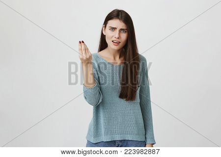 Horizontal portrait of dissatisfied and displeased young woman with dark long hair dressed casually, looking at camera with blue eyes, gesturing actively, frowning face while arguing with boyfriend