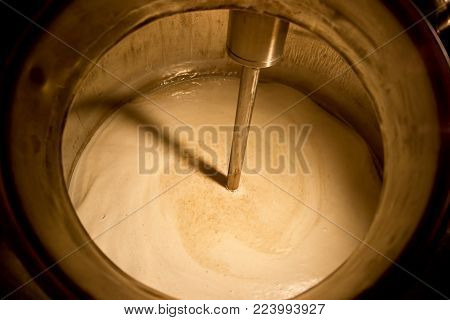 Beer stirring in kettle. Metal stick is stirring a beer in kettle, closeup.