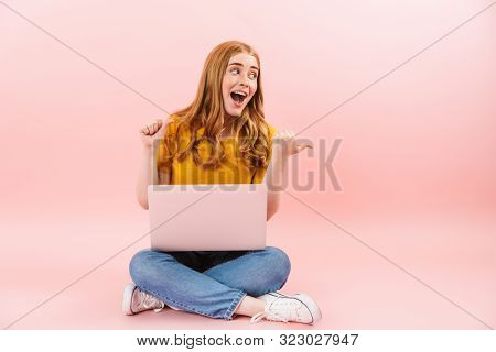 Photo of a young emotional smiling cheery girl isolated over pink wall background using laptop computer showing cpyspace.