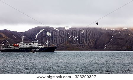 Touristic Antarctic Cruise Liner Following The Black Bird In The Lagoonwith Rocks Of Deception Islan
