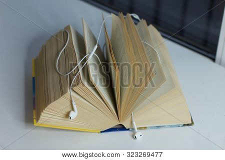 Open Book With Earphones. Electronic Audiobook And Regular Paper Book Concept. Old Versus New.