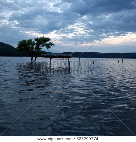 Submerged benches and tree in an artificial lake that has flooded the coast during cloudy golden hour