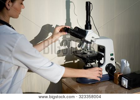 Female Doctor In White Medical Uniform With Stethoscope On Neck Adjusts The Microscope In Laboratory