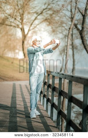 Joyful Stylish Elderly Woman Taking Photo Standing On The Bridge