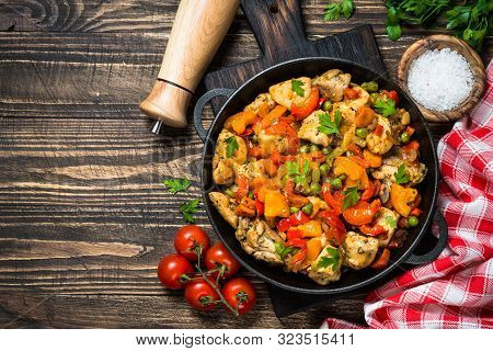 Chicken Stir Fry With Vegetables In Black Iron Plate. Top View On Dark Wooden Background.