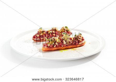 Exquisite serving beef tartare on toast with pickles and black garlic cream on white restaurant plate isolated. High cuisine restaurent dish, minced veal steak meat in minimalist style