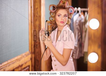 Pretty woman doing a hairstyle in front of the mirror. Dressing room, makeup artist's table. Beauty, fashion concept.