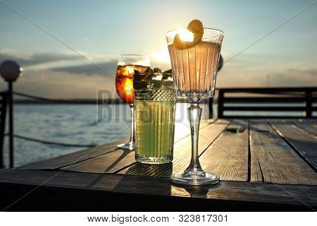 Glasses Of Fresh Summer Cocktails On Wooden Table Outdoors At Sunset