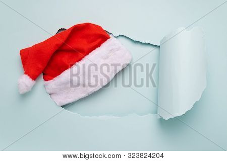 Santa Claus Christmas Hat In A Big Torn Pastel Blue Paper Hole. Minimalism. New Year Concept. Flat L