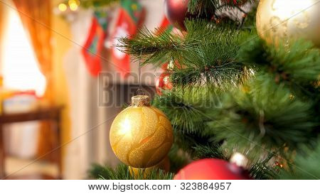 Closeup Image Of Christmas Tree Branch Decorated With Garlands And Golden Baubles Against Firepalce 