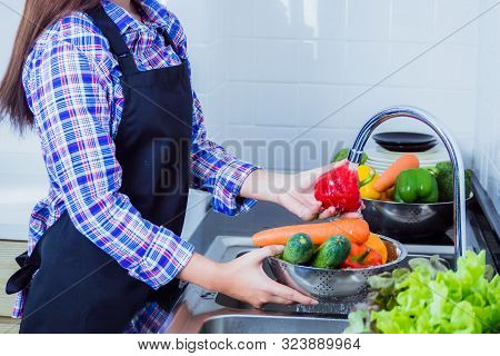 Young Woman Washing Lettuce And Apples To Remove Pesticides Before Cooking In Kitchen. Fruit And Veg