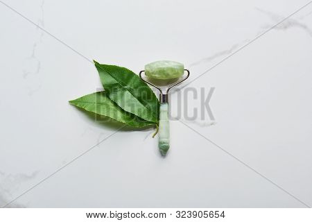 Top View Of Jadeite Facial Roller And Leaves On Marble Surface