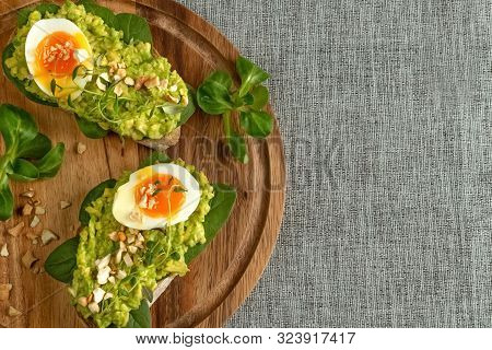 Close Up Of An Avocado Toasts With Soft Boiled Egg, Herbs, Spinach, Salad And Nuts On A Round Wooden