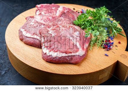 Traditional German raw beef cheeks offered as closeup with herb and spice on a modern design wooden cutting board 